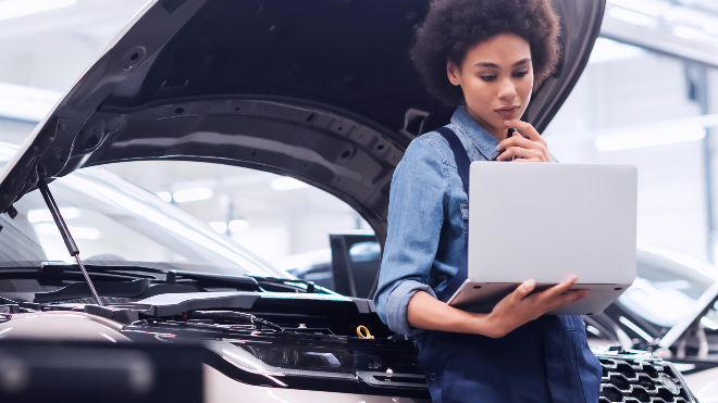 Delphi Technologies Expert sitting on a car bumper using a laptop.